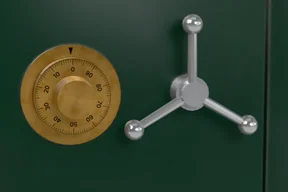 Close-up of the brass combination dial with numbers 0 to 90 and a black index triangle, next to the chrome three-spoke handle on green lacquer
