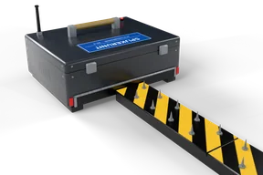 The spike strip leaving the slot at the base of the case: yellow and black links with steel spikes, red reflectors either side of the slot and the red LED lit on the lid